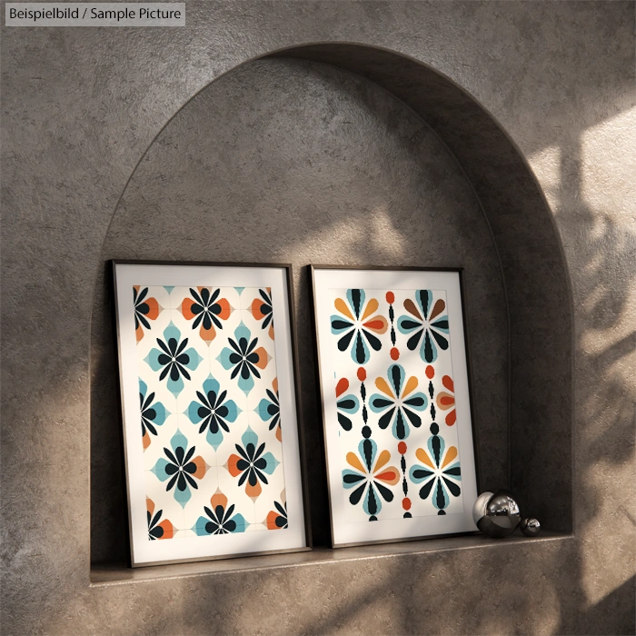 Two framed abstract art pieces with geometric floral patterns in blue, orange, and white on a curved shelf.