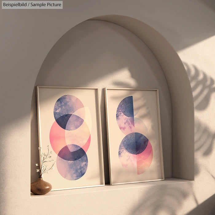 Minimalist art prints with overlapping pink and blue circles on a shelf, under a curved arch with a potted plant.