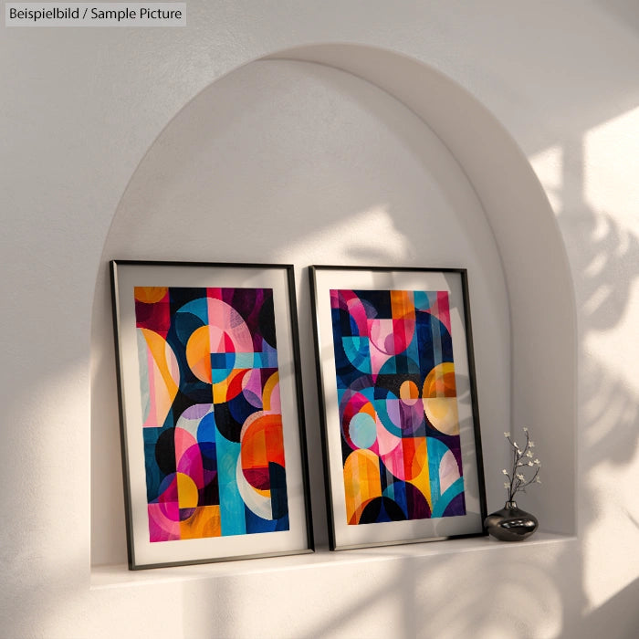 Two colorful abstract paintings on a white arched shelf with shadows and small vase.