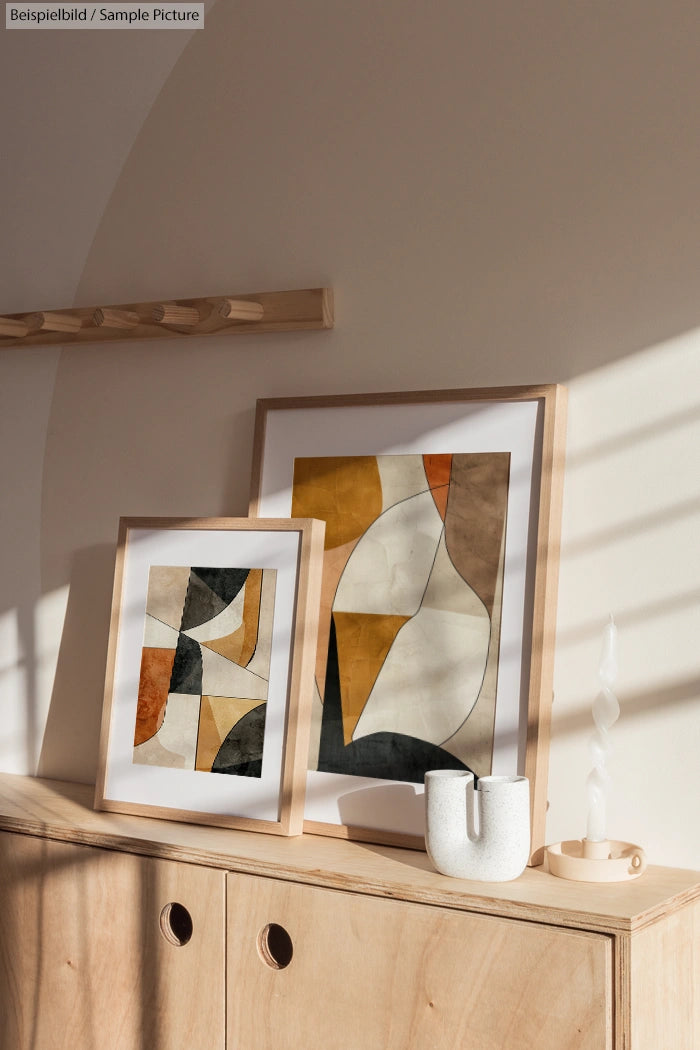 Abstract paintings in wooden frames on a sunlit wooden console, featuring geometric shapes in earthy tones.