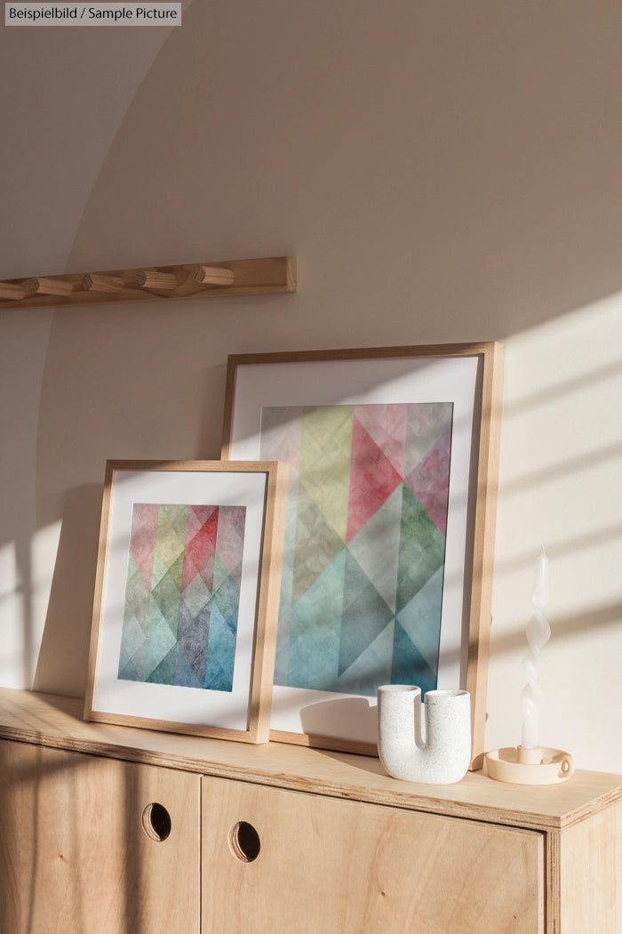 Framed geometric art in pastel colors on wooden cabinet with sunlight and shadows.