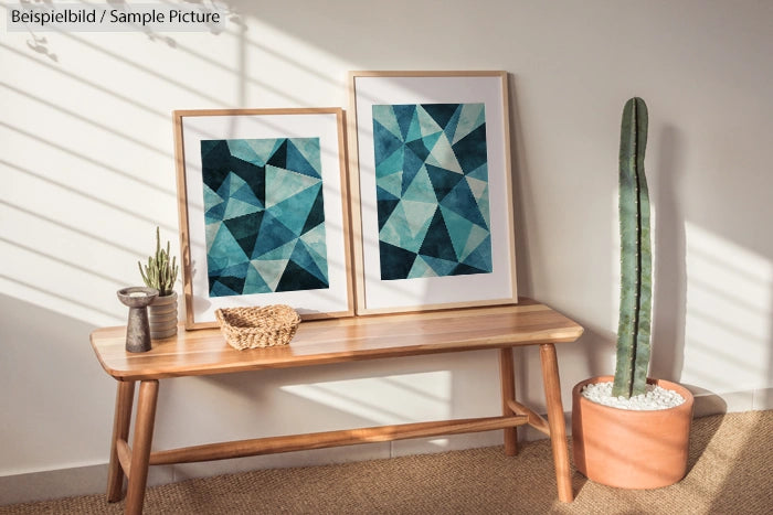 Two geometric art prints on a wooden bench with a cactus plant beside them, in a well-lit room.