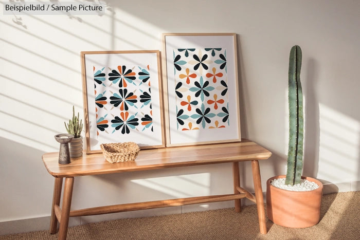 Modern room with two patterned artworks, cactus in terracotta pot, and wooden bench with decorative items.