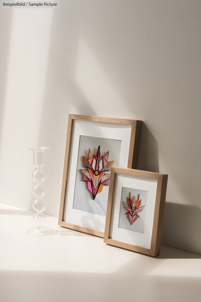 Two framed abstract floral artworks with pink and orange hues, displayed near a clear glass candle holder.