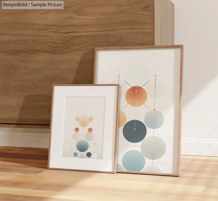 Two framed abstract art pieces with geometric circular patterns leaning against a wooden cabinet in a sunlit room.