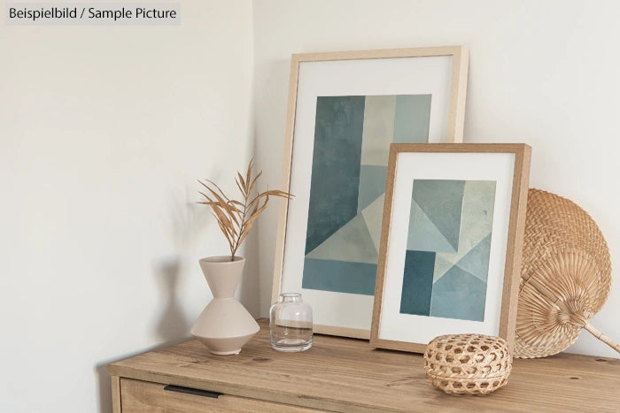 Minimalist decor with abstract geometric prints, vases, and wicker items on a wooden shelf against a white wall.