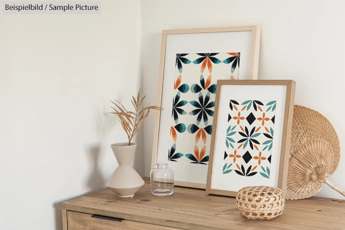 Framed geometric art in orange, black, and teal on wooden sideboard with vase and woven basket.