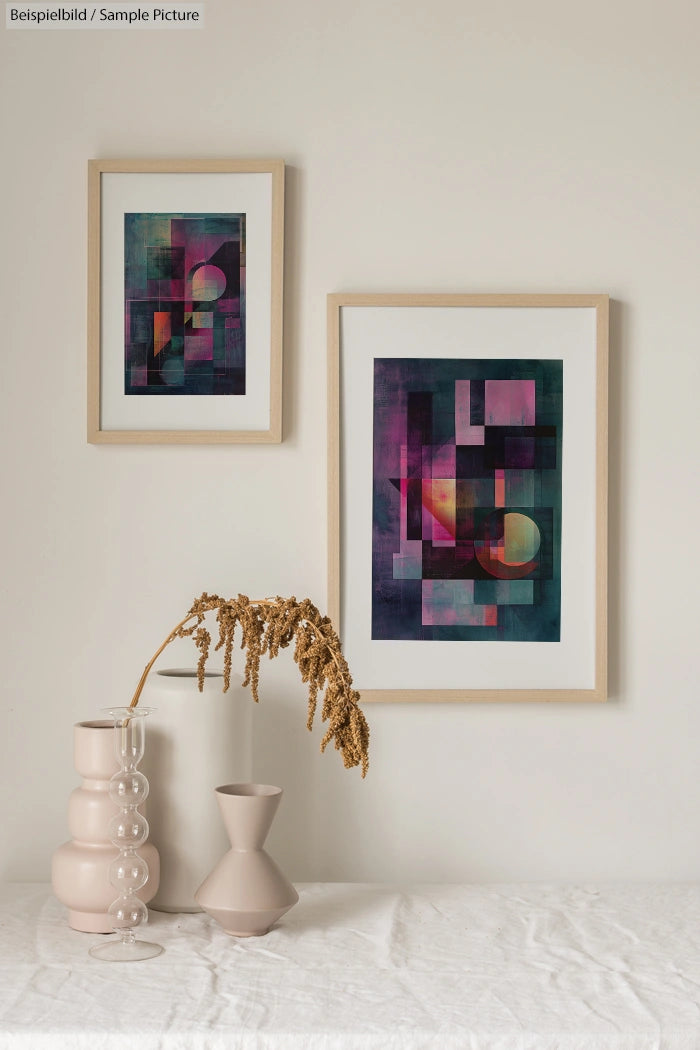 Two framed abstract art pieces with geometric shapes in muted colors above a minimalist table with decorative vases.