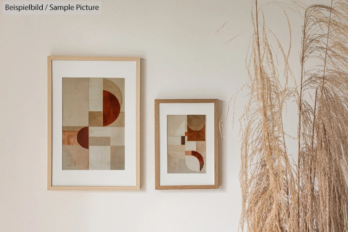 Two framed abstract geometric paintings on a beige wall beside tall dried pampas grass.