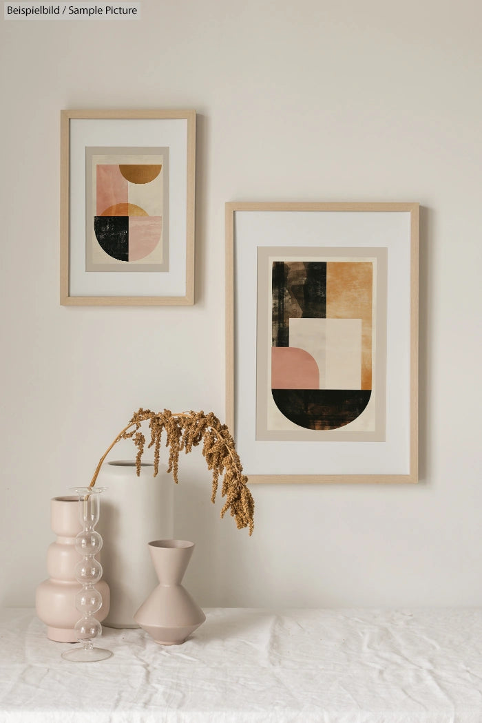 Minimalist interior with abstract paintings, dried plant in glass vase, and ceramic decor on a white table.