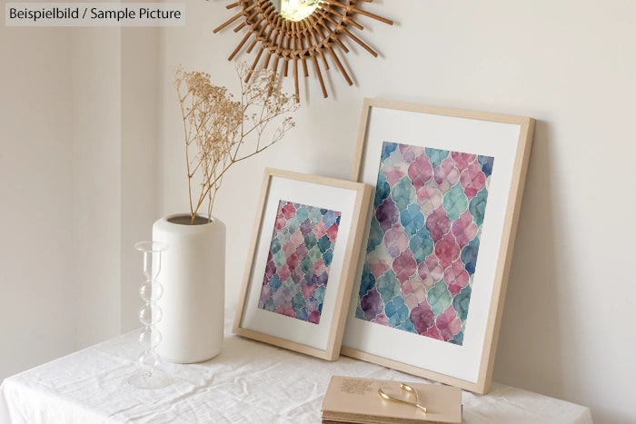 Framed floral geometric artworks on a table with a white vase and dried branches.