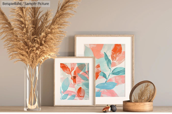 Interior decor with pampas grass vase and abstract leaf paintings on a light wooden surface.