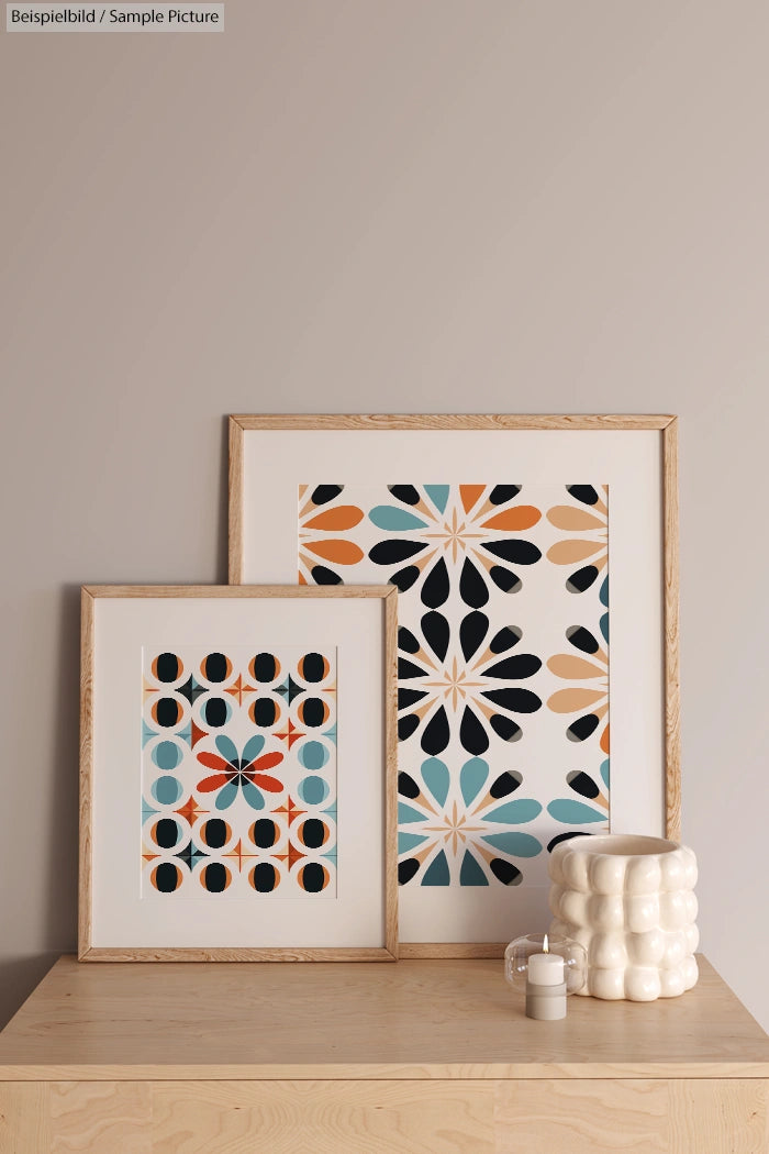 Framed geometric prints with bold patterns on a beige wall above a wooden table with a textured ceramic cup.