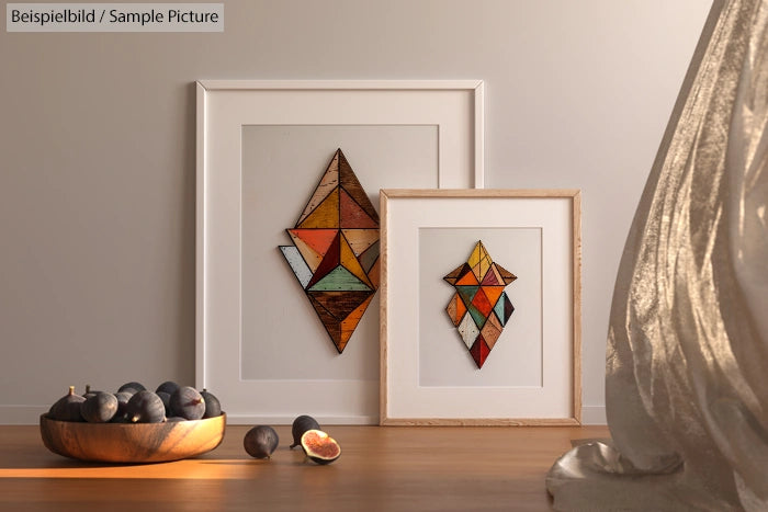 Abstract geometric art in frames beside a bowl of figs on a wooden surface in natural light.