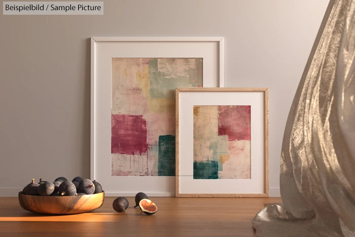 Two abstract paintings with pastel colors in frames, figs in a bowl, draped curtain on right.