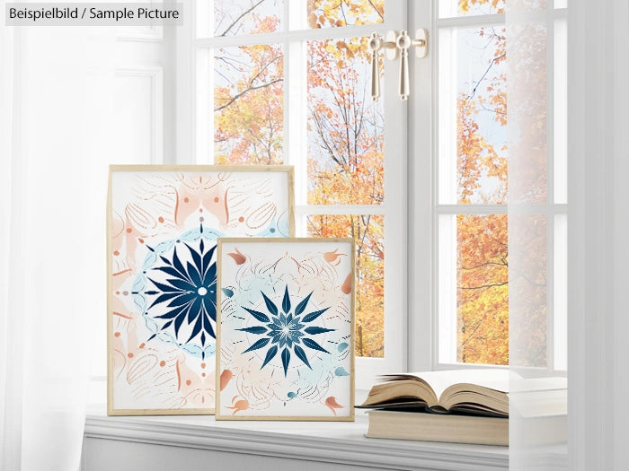 Two framed botanical prints with geometric patterns near a window overlooking autumn trees.