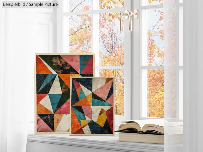 Geometric abstract paintings with triangles on window sill, autumn trees outside.