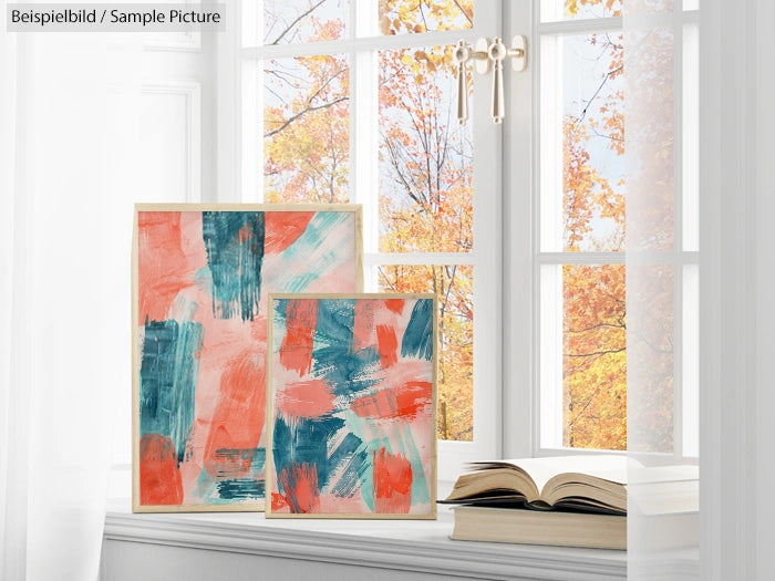 Two abstract paintings with orange and teal brushstrokes on easels by a window; fall foliage visible outside.