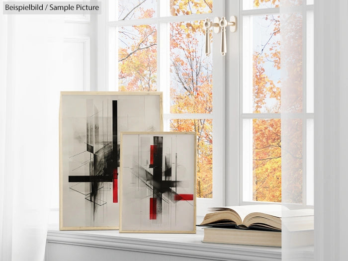 Abstract paintings with black and red shapes on a shelf by a window, with autumn trees visible outside.