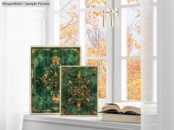 Green and gold ornate notebooks by a window with autumn leaves outside and an open book nearby.