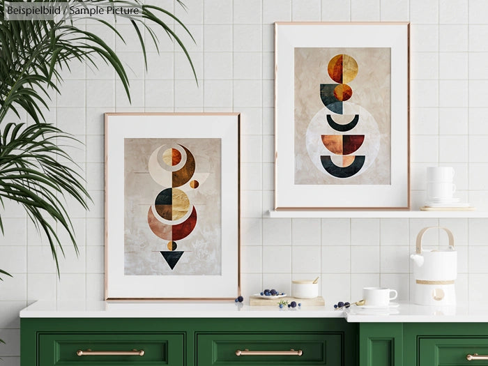 Two abstract geometric art prints with earthy tones on a tiled wall above a green counter with a teapot.