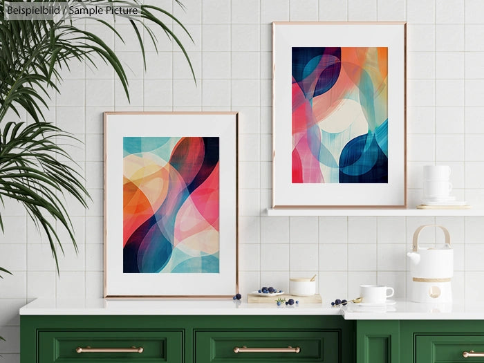 Two abstract paintings with colorful swirls on a white tiled wall above a green cabinet and a white countertop.