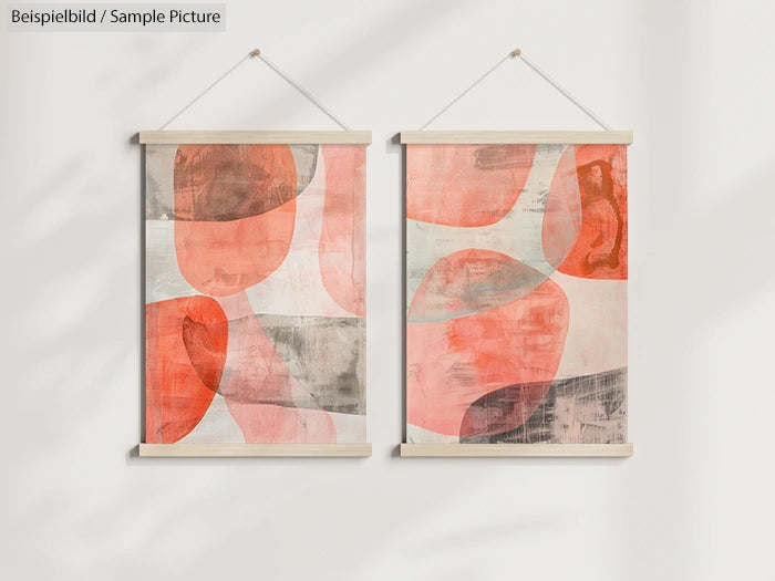 Two abstract paintings with overlapping red and gray shapes, housed in simple wooden frames against a white wall.