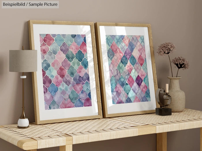 Quilt pattern artwork in frames on a wooden table with small potted plant and gray lamp.