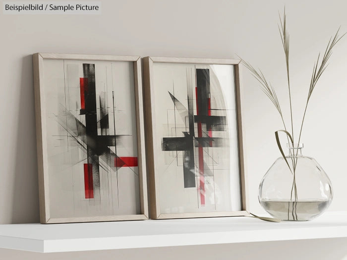 Two abstract paintings with intersecting black and red lines, displayed on a shelf beside a glass vase with reeds.