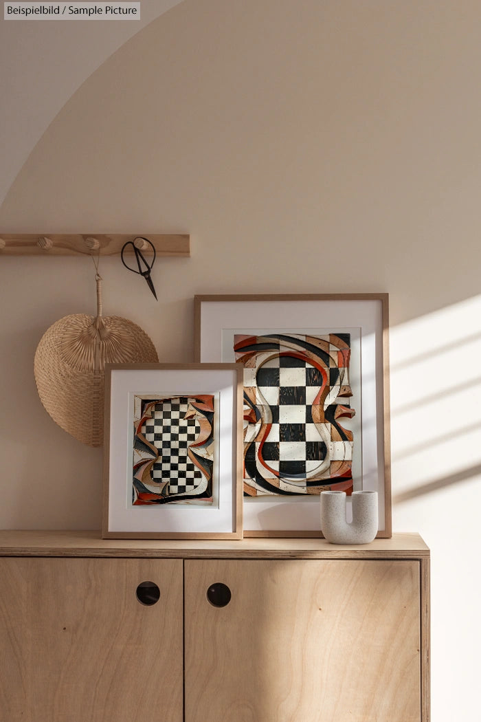 Two framed abstract artworks on cabinet, featuring checkered patterns and flowing lines, light wooden decor, and soft lighting.