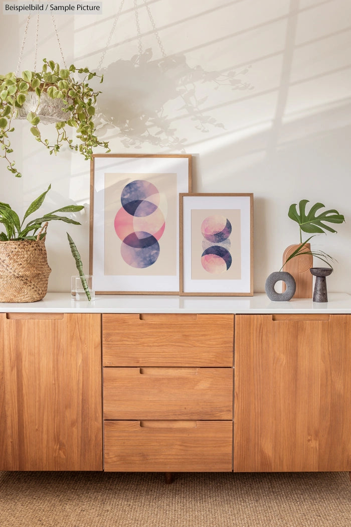 Mid-century modern sideboard with art prints, potted plants, and decor in a sunlit room.