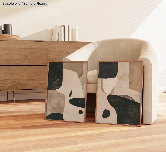 Modern abstract paintings with black and beige patterns leaning against a beige armchair in a bright, minimalistic room.