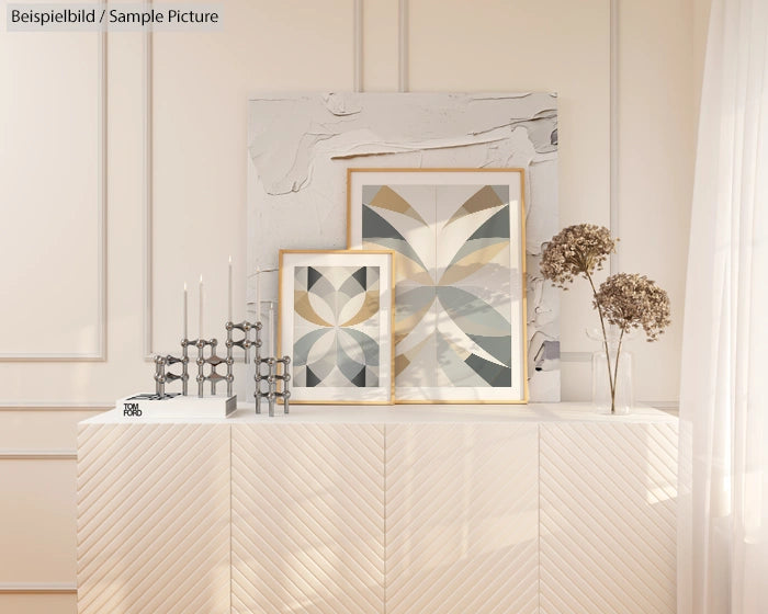 Modern interior with geometric artwork, candles, and dried flowers on a white cabinet against a cream wall.