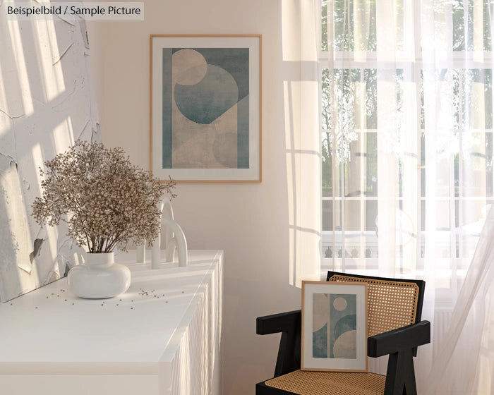 Minimalistic living room with abstract art, wicker chair, and vase with dried flowers on a white sideboard.