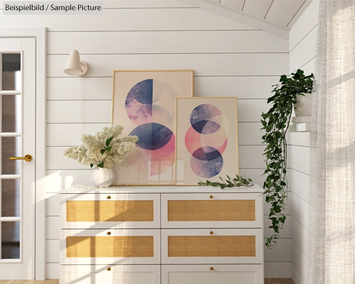 White dresser with wicker drawers, abstract art above it, plant decor, and wooden plank wall in a cozy room.