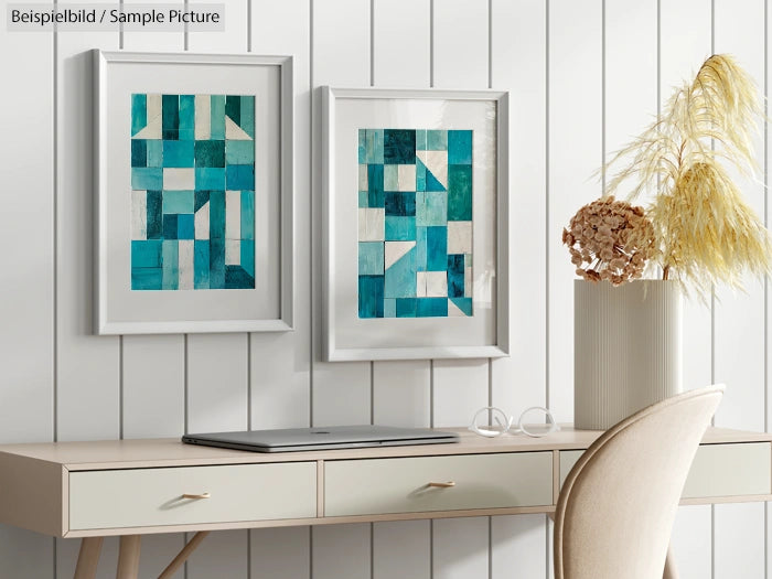 Modern desk with laptop, glasses, and dual abstract blue-green artworks on a white paneled wall.