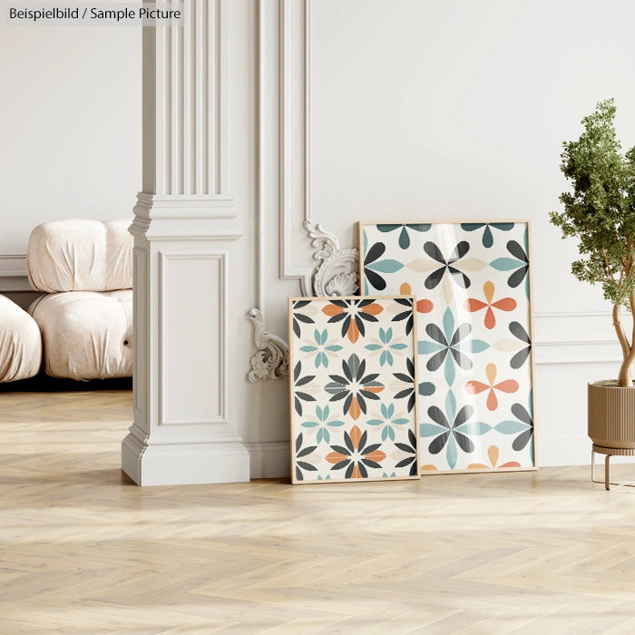 Two framed floral abstract posters leaning against a decorative white column, on a wooden floor beside a potted plant.