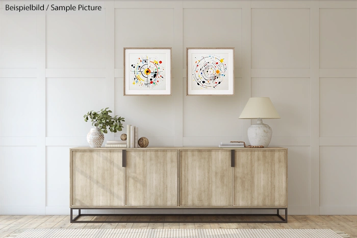 Minimalist living room with two abstract art pieces above a modern wooden sideboard, decorated with a lamp and plant.