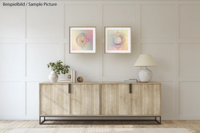 Minimalist living room with wooden sideboard, two abstract art frames, a lamp, and decorative items on display.