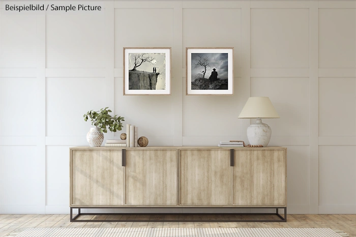 Minimalist living room with light wood sideboard, two framed pictures, a lamp, and a plant in a vase.