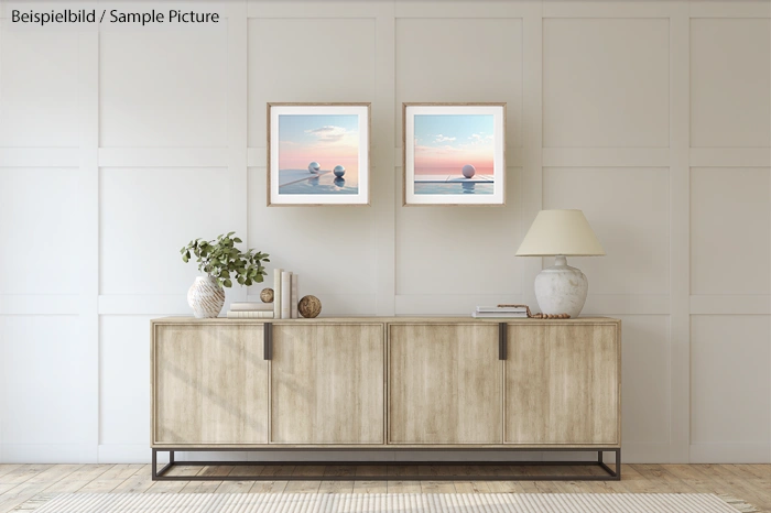 Minimalist living room with wooden sideboard, potted plant, lamp, and two framed prints of ocean scenes on the wall.