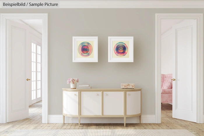 Minimalist living room with two abstract circle paintings above a white console table, soft gray walls, and natural lighting.