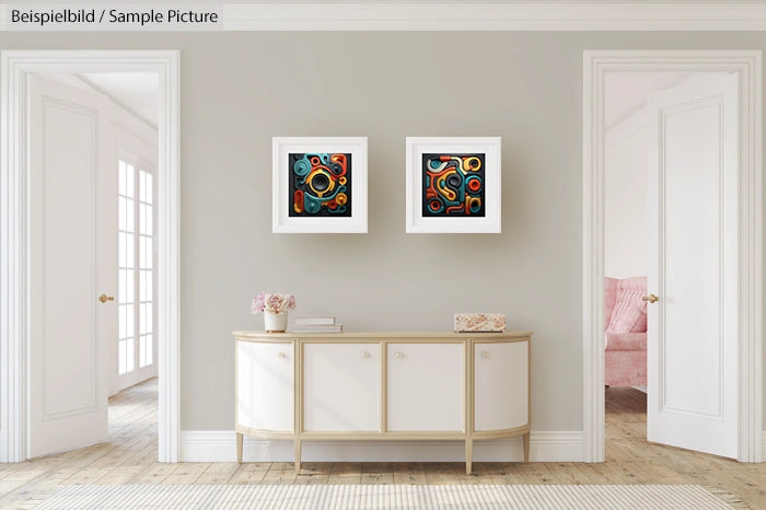 Modern interior with two abstract artworks on wall above a white console table, soft lighting from large windows.