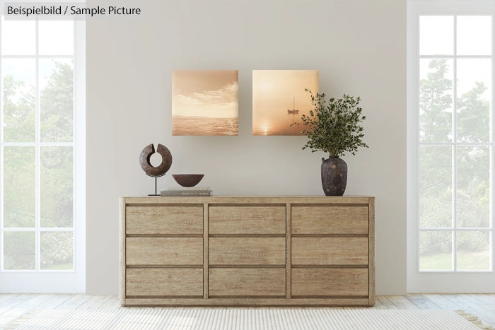 Minimalist living room with wooden sideboard, two square sunset paintings, and a vase with greenery.