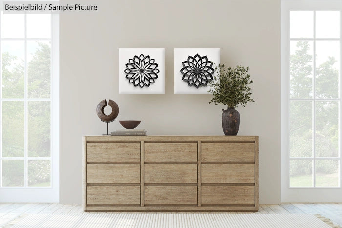 Minimalistic living room with wooden dresser, decorative sculptures, and geometric wall art between two tall windows.