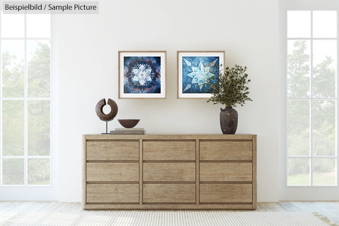 Modern interior with a beige wooden dresser, abstract art, and potted plant against a bright white wall.