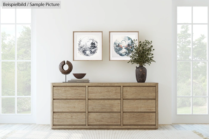 Modern room with wooden dresser, artistic wall prints, and large potted plant; bright natural light through windows.