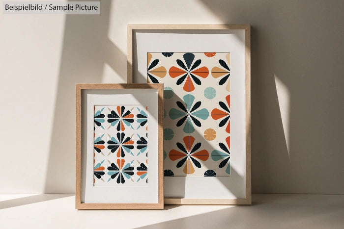 Two framed geometric prints with abstract floral patterns in warm colors, displayed against a textured wall in natural light.