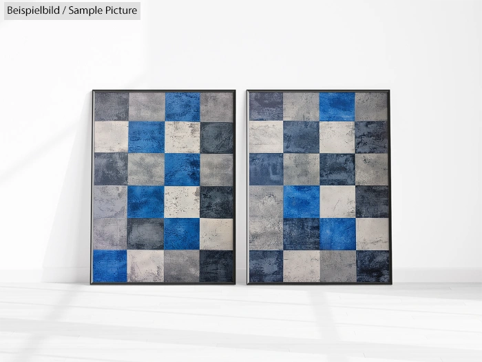 Two abstract paintings with blue, white, and gray checkered patterns leaning against a white wall.