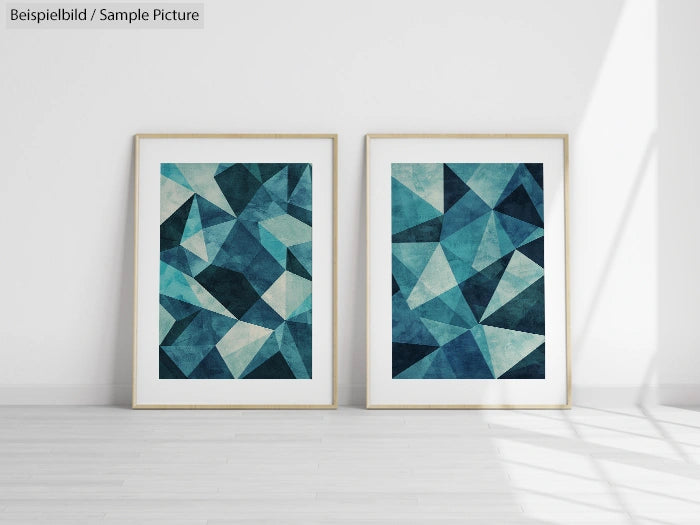 Two framed geometric abstract art pieces in shades of blue, leaning against a white wall on a light wood floor.